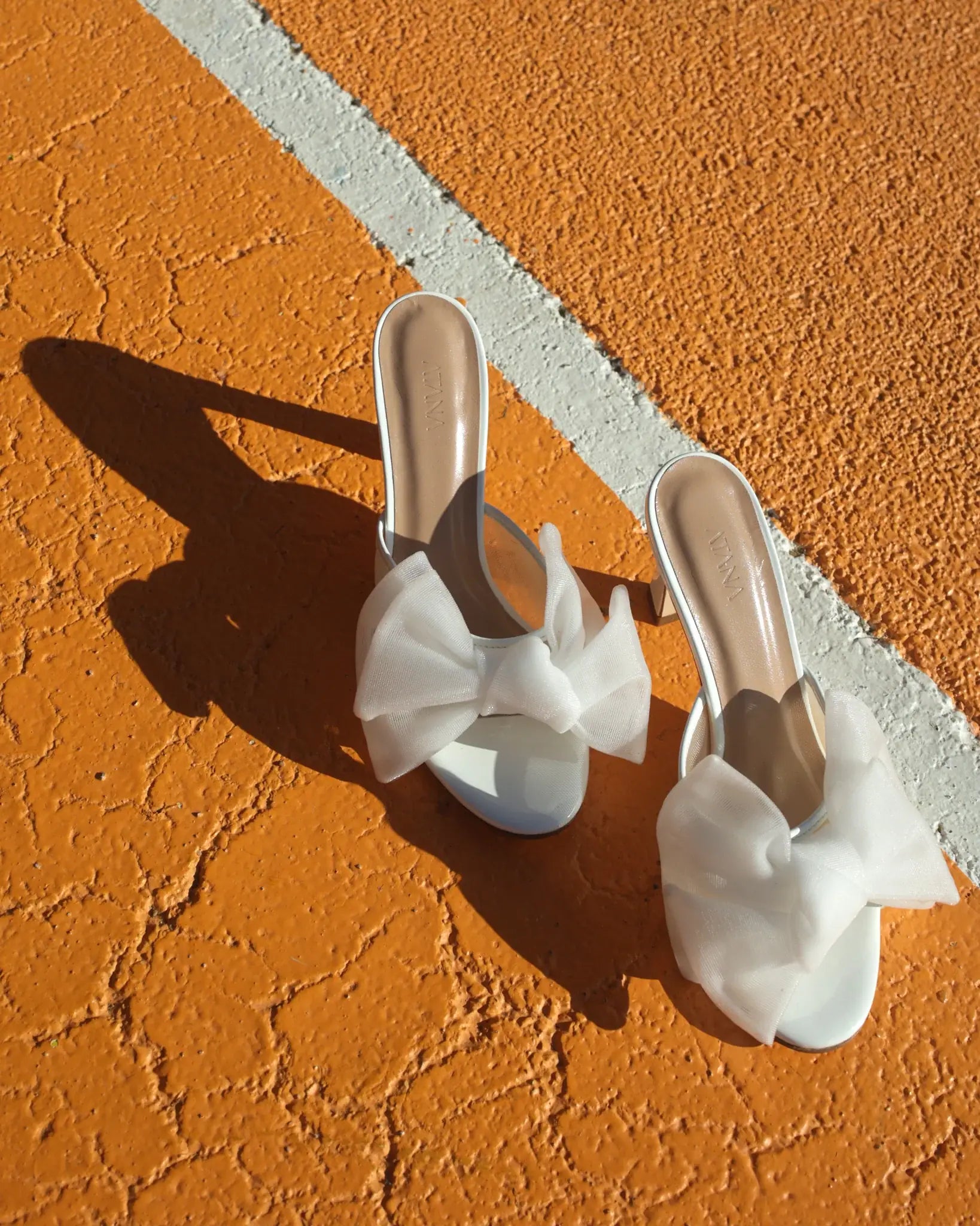 Pair of white sandals with bow details on a textured orange surface