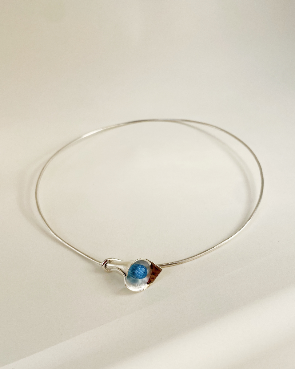 Silver necklace with a blue pendant on a light beige background