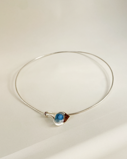 Silver necklace with a blue pendant on a light beige background